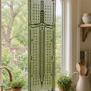 May include: A rectangular olive green crochet curtain panel featuring a central sword motif with geometric patterns, stars, and crescent moons. The piece is suspended from a thin brass rod and displays a grid-like texture throughout the design.