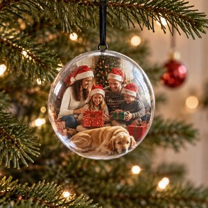 May include: A clear, spherical glass Christmas ornament featuring a printed photograph of a family of four and a golden retriever dog wearing Santa hats while opening wrapped gifts in front of a decorated Christmas tree, suspended by a black ribbon.