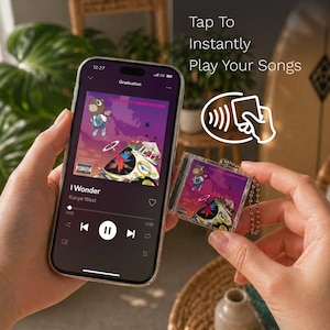 May include: A smartphone displaying a music streaming interface with the album art for Graduation by Kanye West, alongside a small, square, clear acrylic keychain featuring the same album artwork and a metal ball chain, with text reading Tap To Instantly Play Your Songs.