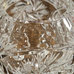 May include: Close-up of a clear, cut-glass bowl. The bowl features intricate etched patterns of radiating lines and leaf-like designs. The glass reflects light, creating a sparkling effect. The bowl's design suggests it could be used for decorative purposes.