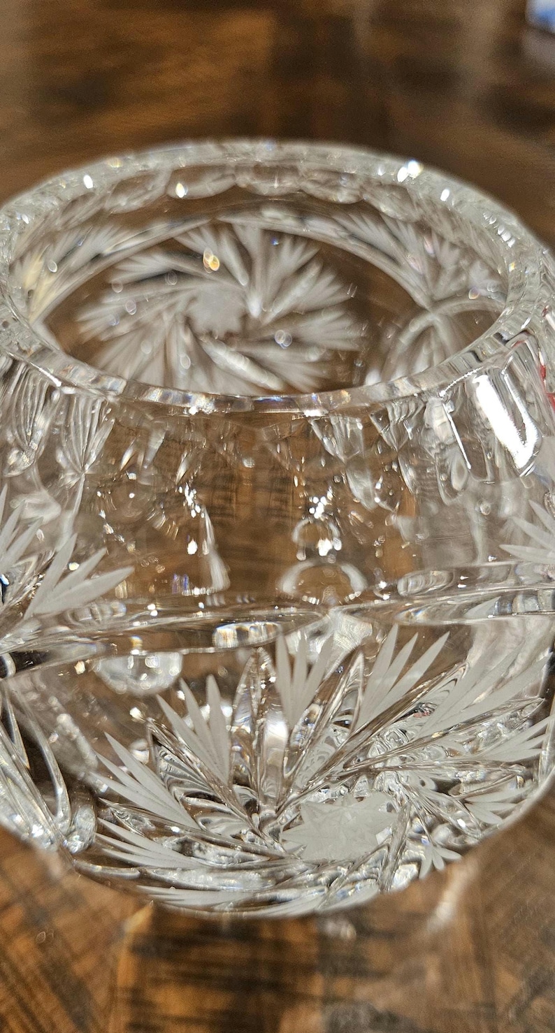 May include: Close-up of a clear, cut-glass bowl. The bowl features intricate etched patterns of radiating lines and leaf-like designs. The glass reflects light, creating a sparkling effect. The bowl's design suggests it could be used for decorative purposes.