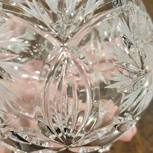 May include: A clear, cut-glass bowl with a detailed, symmetrical floral pattern. The bowl has a rounded shape and sits on small feet. The intricate design reflects light, creating a sparkling effect. The bowl is likely used for decorative purposes.