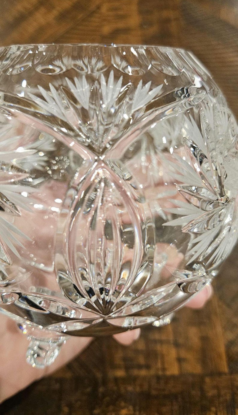 May include: A clear, cut-glass bowl with a detailed, symmetrical floral pattern. The bowl has a rounded shape and sits on small feet. The intricate design reflects light, creating a sparkling effect. The bowl is likely used for decorative purposes.