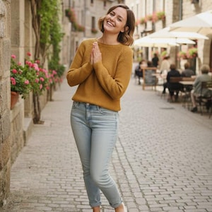 Puede incluir: Una persona con un suéter amarillo mostaza, jeans azul claro y zapatillas a cuadros en blanco y negro. Está de pie en una calle adoquinada frente a un edificio de piedra con flores y un restaurante.
