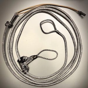 May include: A black and white braided rope with a loop and a knot at one end. The rope is coiled and has a brown cord attached. The rope is likely used for training or handling animals.