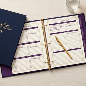 以下が含まれることがあります： 金色の十字架のエンブレムが付いた、The Pastor's Ministry Plannerというタイトルの紺色の3リングバインダー。開いたプランナーには、紫色のアクセントが付いた週ごとのスケジュールと振り返りのページが表示されており、タブで整理され、金色のボールペンが添えられています。