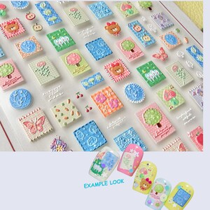 May include: A sheet of colorful nail art stickers featuring various designs, including teddy bears, trees, flowers, and butterflies. The stickers are in a variety of pastel colors and have a 3D embossed effect. The phrase "EXAMPLE LOOK" is also visible.