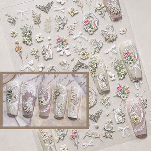 May include: A sheet of adhesive nail art stickers featuring embossed designs of cherubs, floral bouquets, ornate oval frames, bows, and lace patterns. The collection includes individual decals and five pre-decorated artificial nail tips.