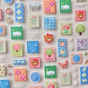 May include: A collection of colorful, textured stickers featuring various designs. The stickers include images of apples, trees, flowers, bears, butterflies, and geometric patterns. The color palette includes pink, green, blue, orange, and white.