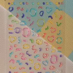 May include: A sheet of colorful, 3D gel stickers. The stickers feature various shapes, including hearts, circles, and squiggly lines, in shades of pink, yellow, blue, green, and purple. The stickers are on a clear, transparent sheet.