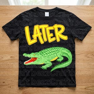 May include: Black t-shirt with a green alligator graphic and the word "LATER" in yellow, cartoon-style lettering. The alligator has a red mouth and is set against a black background. A fun, casual tee.