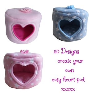 May include: Three soft, plush pet pods with heart-shaped openings and a small top handle. One is solid pink, one is blue with white stars, and one is pink with white stars. Text reads: 50 Designs create your own cosy heart pod XXXXX.