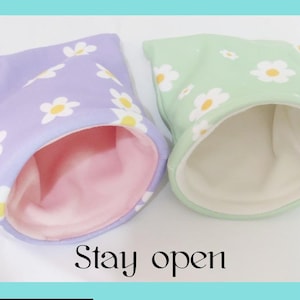 May include: Two small pet beds, one lavender and one mint green, each with a daisy pattern. The beds have a soft, plush interior and a rolled-over opening. The text "Stay open" is at the bottom.