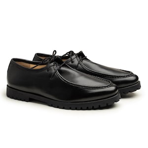 Puede incluir: Un par de zapatos de cuero negro con un diseño clásico. Los zapatos tienen una puntera redondeada, cierre con cordones y una suela gruesa y texturizada. Los zapatos están hechos de cuero liso y pulido.