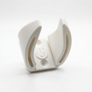 May include: A white 3D-printed holder with a curved design. The holder features a circular emblem and two curved slots. The object is designed to hold a specific item, likely a lightsaber or similar prop.