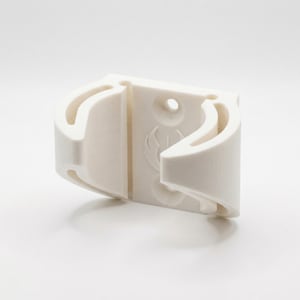May include: A white, 3D-printed object with curved, open sections and a central, solid panel. The panel features a circular hole and a stylized emblem. The object appears to be a holder or mount, possibly for a specific item.