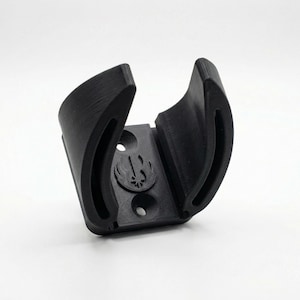 May include: A black 3D-printed lightsaber wall mount. The mount features a curved design to cradle the hilt, with a symbol of a bird and a star. It has two holes for mounting.