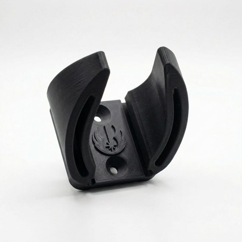 May include: A black 3D-printed lightsaber wall mount. The mount features a curved design to cradle the hilt, with a symbol of a bird and a star. It has two holes for mounting.