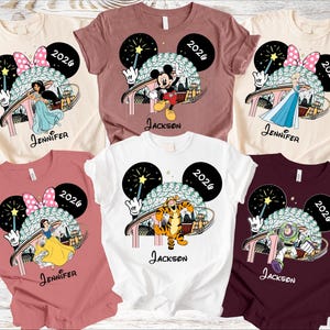 May include: Assorted-color t-shirts featuring Disney characters like Mickey Mouse, Jasmine, Elsa, Snow White, Tigger, and Buzz Lightyear. Each shirt has a 2026 graphic and a name. The shirts are a variety of colors, including white, pink, and burgundy.