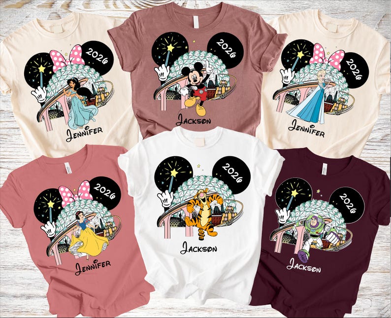 May include: Assorted-color t-shirts featuring Disney characters like Mickey Mouse, Jasmine, Elsa, Snow White, Tigger, and Buzz Lightyear. Each shirt has a 2026 graphic and a name. The shirts are a variety of colors, including white, pink, and burgundy.