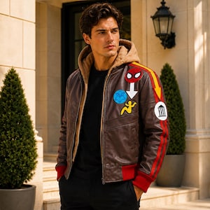 May include: A brown leather jacket featuring a tan hood, red ribbed cuffs, and a red and yellow stripe down the sleeve. The jacket is decorated with various patches, including a Spider-Man mask, a blue circular emblem, and a white circular patch.