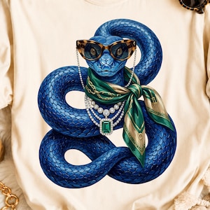 Könnte beinhalten: Ein cremefarbenes T-Shirt mit einer Grafik einer geringelten blauen Schlange, die eine Katzenaugenbrille mit Leopardenmuster, ein grünes Seidentuch und eine mehrlagige Halskette mit einem großen rechteckigen grünen Edelsteinanhänger trägt.