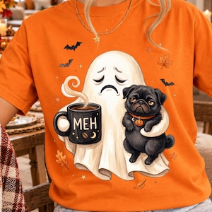Könnte beinhalten: Ein orangefarbenes T-Shirt mit einer Grafik eines traurigen Geistes, der eine schwarze Tasse mit der Aufschrift MEH hält, sowie einem schwarzen Mops mit orangefarbenem Halsband und Kürbisanhänger. Das Design zeigt kleine Fledermäuse und Blätter.
