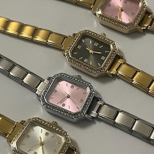 May include: Four rectangular-faced watches with gold and silver bands. The watch faces are pink, silver, and dark gray, each with a diamond-studded bezel. The watch hands are gold.