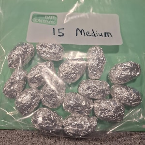May include: A clear plastic storage bag containing fifteen individual items wrapped in shiny silver aluminum foil. A white label on the bag features the printed text DATE: CONTENTS: and the handwritten text 15 Medium in black ink.