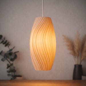 May include: A cream-coloured pendant light with a swirling, textured pattern. The oval-shaped light hangs from a white cord and emits a warm glow. The background features a wooden surface and decorative plants. The light is approximately 25 cm in height.