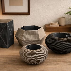 Pode incluir: Uma coleção de vasos decorativos em várias formas e tamanhos. Os vasos são em tons neutros de preto e bege, com designs geométricos texturizados. Uma pequena planta em vaso e uma lâmpada tecida também são visíveis.