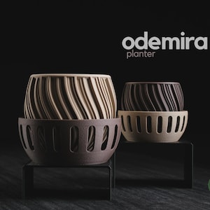 Peut inclure: Deux jardinières étiquetées odemira planter. La jardinière de gauche possède un pot intérieur beige à motifs torsadés dans une coque extérieure marron foncé avec des découpes verticales. Celle de droite a un pot marron foncé dans une coque beige.