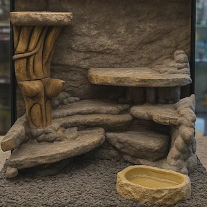 May include: A terrarium background insert featuring a multi-level rock formation with a tall, textured tree-like pillar on the left, several flat stone-like platforms at varying heights, and a separate, small, oval-shaped stone-coloured feeding dish.