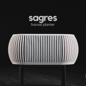 Puede incluir: Una maceta para bonsái blanca con forma de barril y un diseño de listones verticales. El texto 'sagres bonsai planter' está impreso sobre el objeto, y un pequeño logotipo circular verde con el texto 'h3liø design' es visible en la esquina inferior derecha.