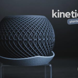 Op de afbeelding: Een donkergrijze bolvormige plantenbak met een complex, herhalend geometrisch rasterpatroon. De plantenbak staat op een bijpassende schotel met textuur. De tekst "kinetic planter" staat rechtsboven en een klein "h3liø design" logo is zichtbaar.
