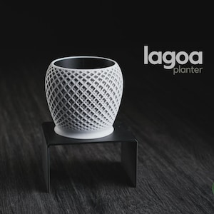 Peut inclure: Un pot de fleurs blanc de forme sphérique avec un motif en treillis ouvert complexe. Le pot présente un bord circulaire lisse et une base solide. Le texte 'lagoa planter' est visible en haut à droite, et un logo circulaire 'h3liø design' est en bas à droite.