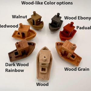 Pu&ograve; includere: Una collezione di piccoli oggetti decorativi a forma di barca in vari colori effetto legno. Le opzioni di colore includono Noce, Redwood, Ebano, Paduak, Dark Wood Rainbow, Legno e Venatura del legno. Il testo "Wood-like Color options" &egrave; in alto.