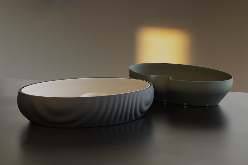 Pu&ograve; includere: Due moderne ciotole ovali in ceramica. Una &egrave; grigio scuro con un motivo testurizzato a forma di onda all'esterno e un interno bianco. L'altra &egrave; verde oliva con una finitura liscia. Entrambe sono su una superficie scura.