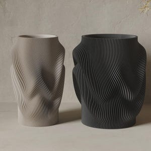 Puede incluir: Dos jarrones cilíndricos, uno en beige claro y otro en gris carbón oscuro, con una textura acanalada vertical distintiva y un patrón ondulado que crea una sensación de movimiento en la superficie exterior de cada recipiente.