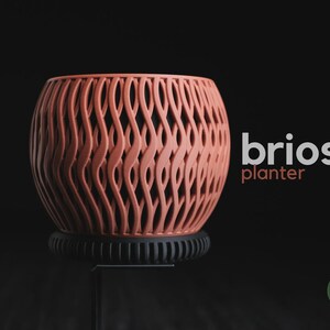 May include: A terracotta-coloured planter with a complex, vertical wave-like lattice pattern. The planter sits on a black, ribbed circular base. The text "briosi planter" appears to the right, and a small green circular logo reads "h3liø design".