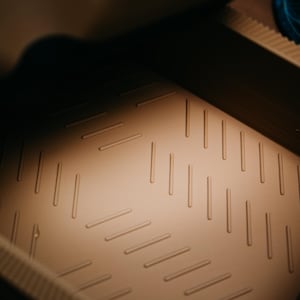 May include: A close-up shot of a tan, rectangular container interior. The base features a textured pattern of diagonal, parallel lines. The lighting creates shadows, highlighting the texture and shape of the container.