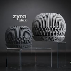 Puede incluir: Dos maceteros esféricos grises con un patrón geométrico de celosía y platos a juego. El texto 'zyra planter' aparece en la parte superior izquierda y un logotipo circular 'h3liø design' está en la esquina inferior derecha.