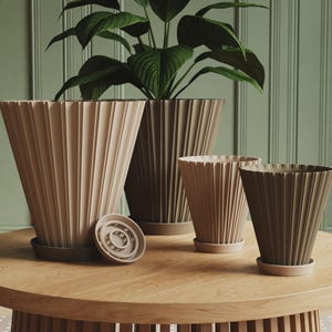 May include: A collection of four conical plant pots with a vertical pleated texture. The pots come in varying shades of beige and brown, each featuring a matching circular saucer base. One small circular insert is placed separately on the surface.