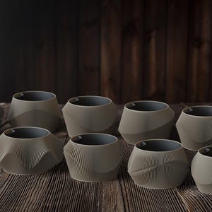May include: A collection of eight gray ceramic planters with a textured, ribbed design. The planters have a geometric shape and a dark gray interior. They are arranged on a wooden surface.
