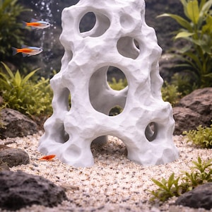 Peut inclure: Décoration d'aquarium blanche et poreuse en forme de formation rocheuse avec de multiples ouvertures. L'ornement est dans un aquarium avec du gravier, des plantes et de petits poissons. Les poissons sont orange et bleu.
