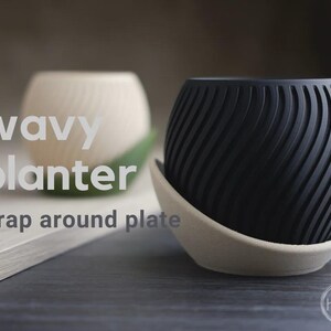Peut inclure: Un pot de fleurs sphérique noir avec une surface ondulée texturée reposant dans une assiette incurvée beige clair. Le texte wavy planter wrap around plate est visible sur le côté gauche de l'image, et un petit logo circulaire est présent.