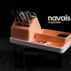 May include: A peach-colored desk organizer with multiple compartments for pens, scissors, and small items, featuring a white base and the text navais organiser printed in white and peach on the upper right side of the frame.