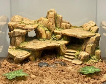Puede incluir: Decoración de terrario multinivel detallada en tonos marrones y beige, que se asemeja a un paisaje rocoso con plataformas, arcos y escalones. Los acentos de musgo verde añaden un toque de color. Ideal para hábitats de reptiles.