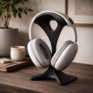 Puede incluir: Auriculares supraaurales blancos y grises sobre un soporte negro para auriculares. El soporte tiene un diseño curvo único. Los auriculares tienen almohadillas grises y una diadema blanca. El soporte está sobre una superficie de madera.
