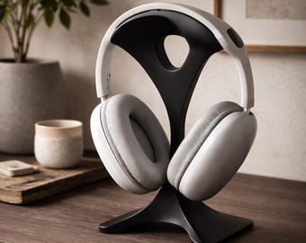 May include: A pair of white over-ear headphones with light gray cushioned ear pads resting on a black, curved, Y-shaped stand. The headphones feature a smooth white headband and a solid black interior frame, providing a stable display for the device.